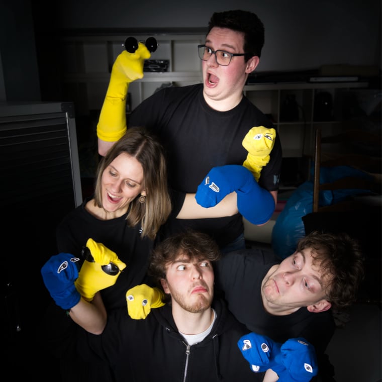 Lachende Personen mit gelben und blauen Handpuppen.